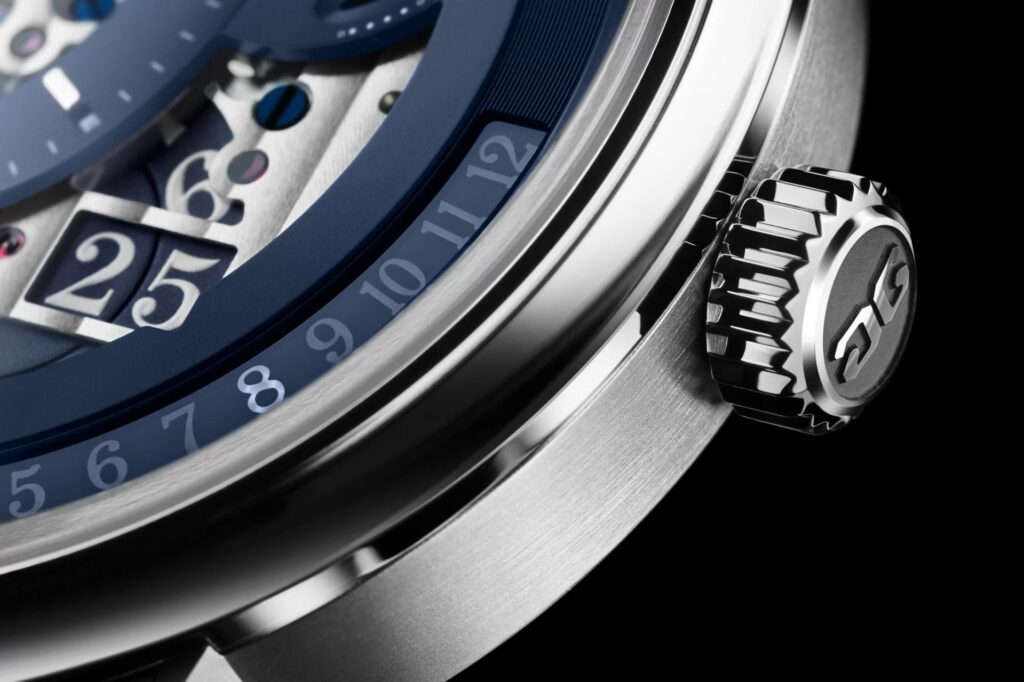 dettaglio corona zigrinata di un Glashütte Original PanoMaticCalendar Skeleton "Blue of Dawn", realizzata in platino, affiancata da una porzione del quadrante scheletrato blu. Visibili ci sono una fascia con le indicazioni retrograde del mese e parte della doppia finestra panoramica della data